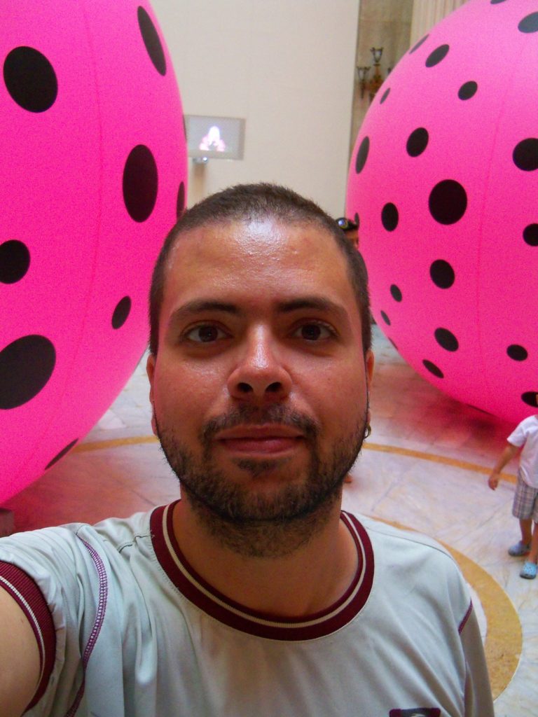 Foto do escritor Guilherme Fraenkel entre bolas rosas gigantes no CCBB do Rio de Janeiro